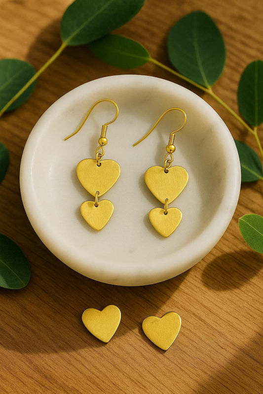 Gold heart-shaped earrings on a white dish with green leaves in the background