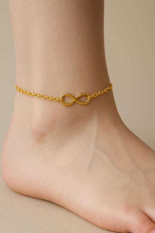 Gold anklet with an infinity symbol on a foot against a neutral background