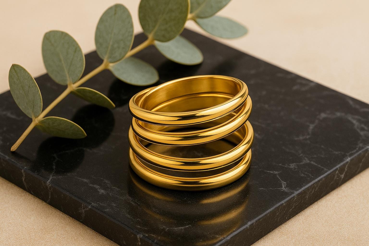 Stack of gold rings on a black marble surface with green leaves.