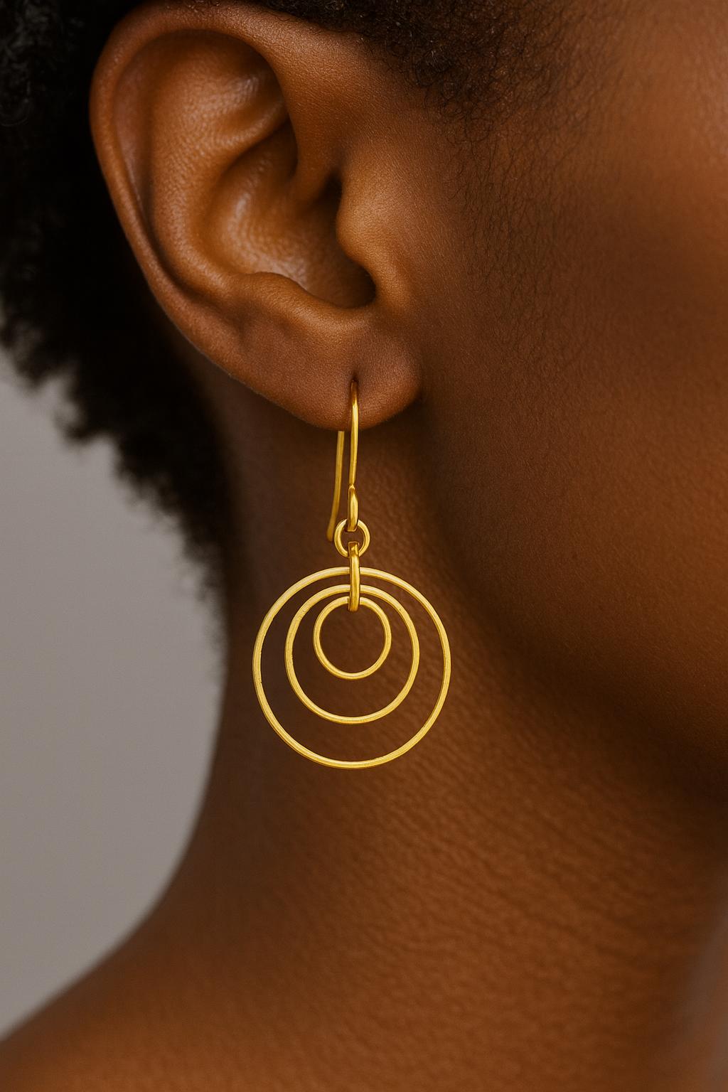 Gold Brass Dangle earrings on a textured surface with a black box in the background