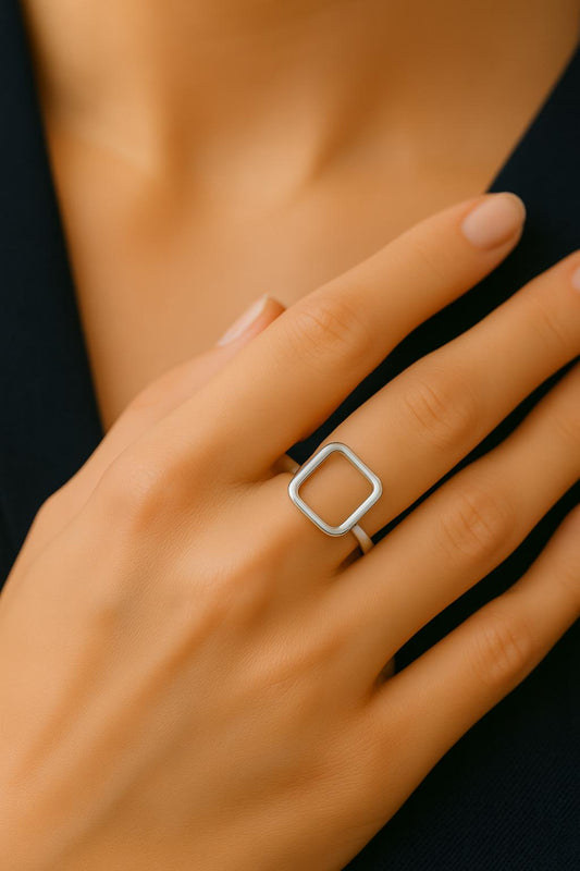 Silver square ring on a hand against a black background