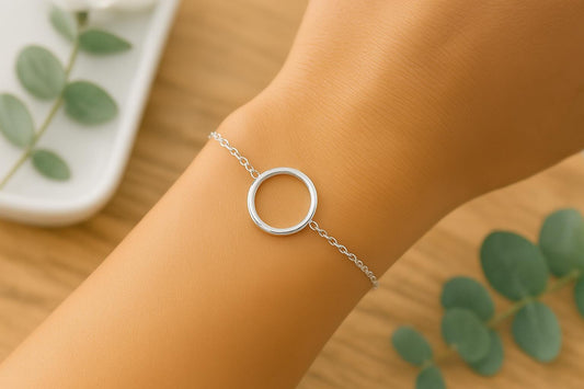 Silver bracelet with a circular design on a wrist, with green leaves in the background.