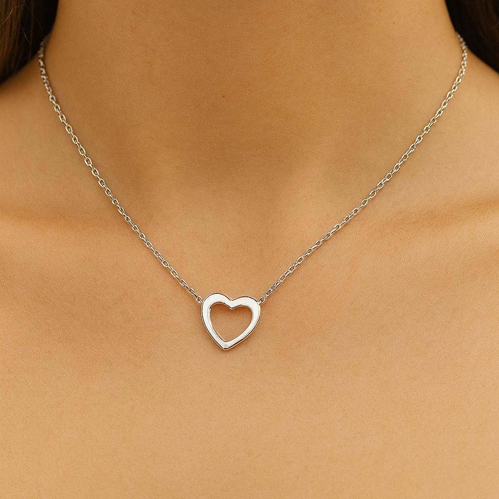 Silver heart-shaped necklace on a person's neck against a neutral background