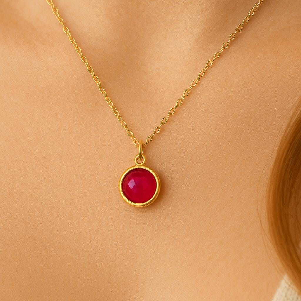 Gold necklace with a red ruby pendant on a person wearing a beige top.