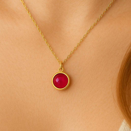 Gold necklace with a red ruby pendant on a person wearing a beige top.