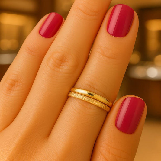 Hand with red nail polish wearing a gold ring set in smooth and sparkle texture against a blurred background