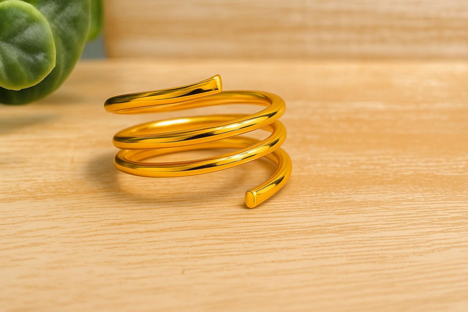 Gold spiral ring on a wooden surface with a plant in the corner