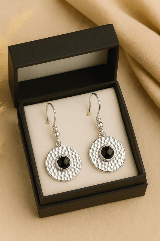 Silver earrings with black centers in a black box on a beige fabric background