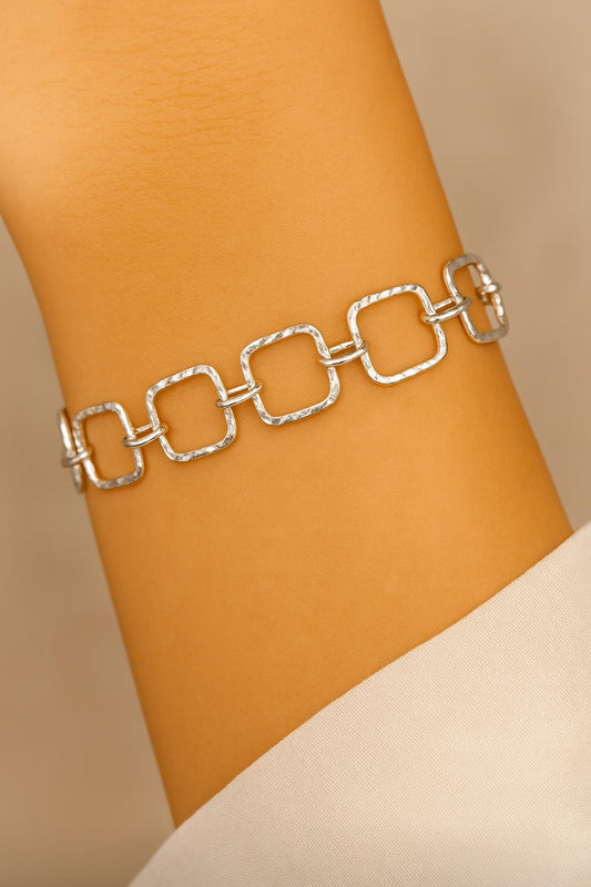 Silver chain bracelet on a wrist against a beige background