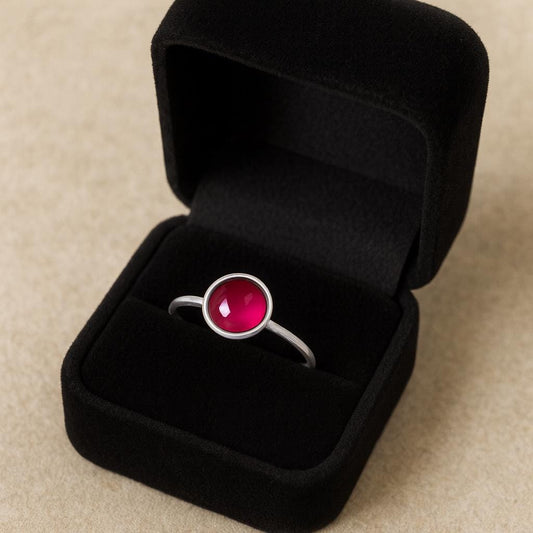 Silver ring with a red ruby gemstone in a black jewelry box on a beige background