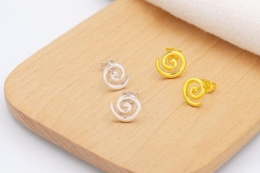 Pair of spiral-shaped earrings, one gold and one silver, on a wooden surface.