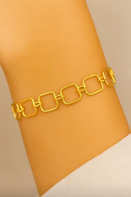 Gold chain bracelet on a wrist with a neutral background
