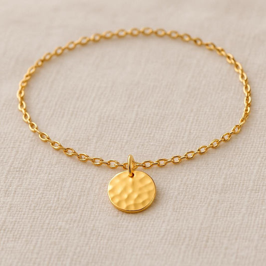 Gold bracelet with a round pendant on a beige background