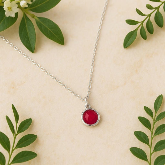 Necklace with a red ruby pendant on a silver cable chain and beige background with green leaves