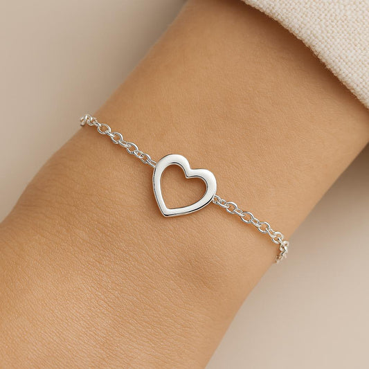 Silver heart-shaped bracelet on a wrist against a neutral background