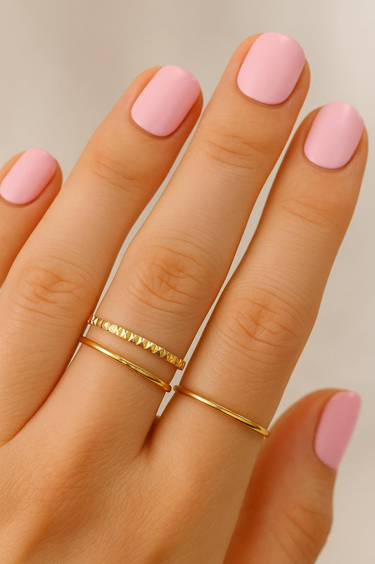 Hand with pink nails and gold rings on a neutral background