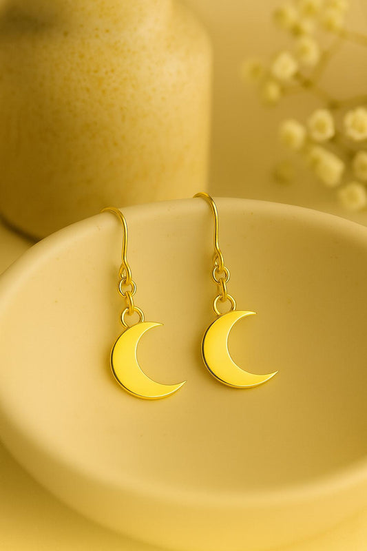 Gold crescent moon earrings on a yellow plate with a blurred background