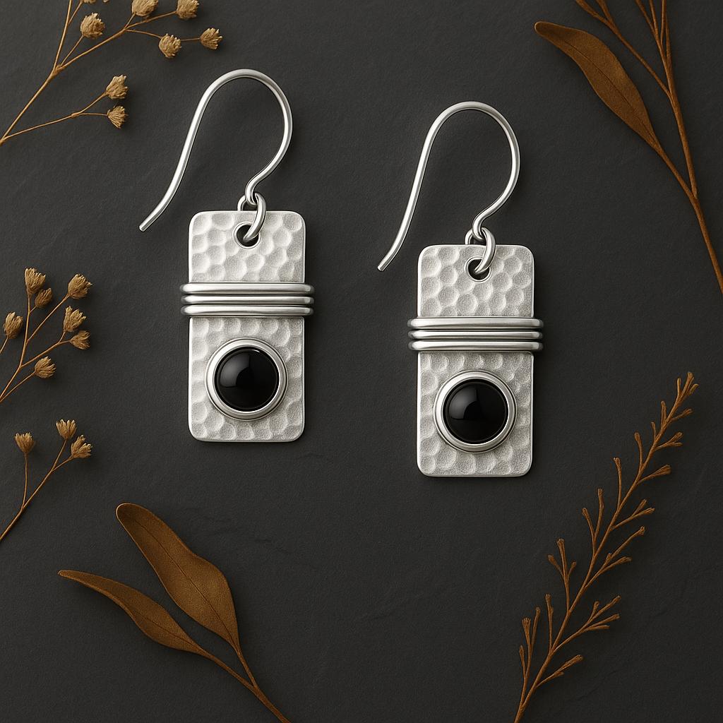 Pair of silver earrings with black stones on a dark background with dried leaves.