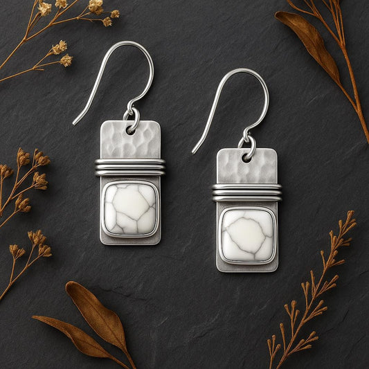 Silver earrings with white stone on a dark surface with dried leaves.