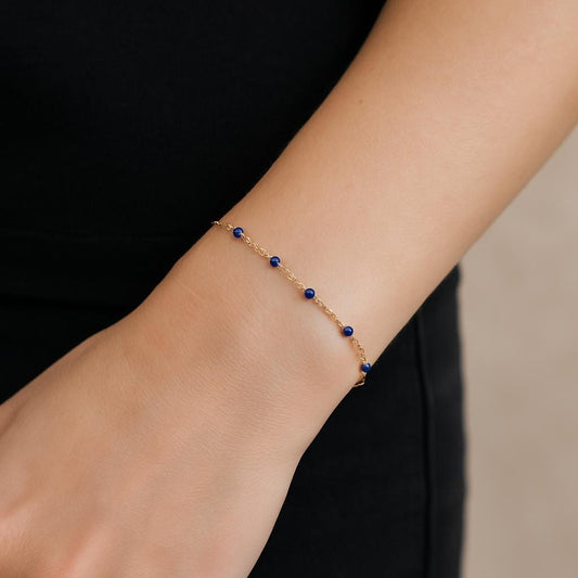 Gold bracelet with blue beads on a wrist against a black background