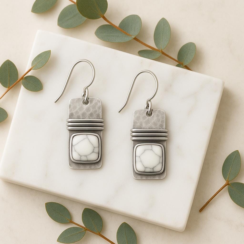 Pair of silver earrings with marble-like design on a marble surface with green leaves.