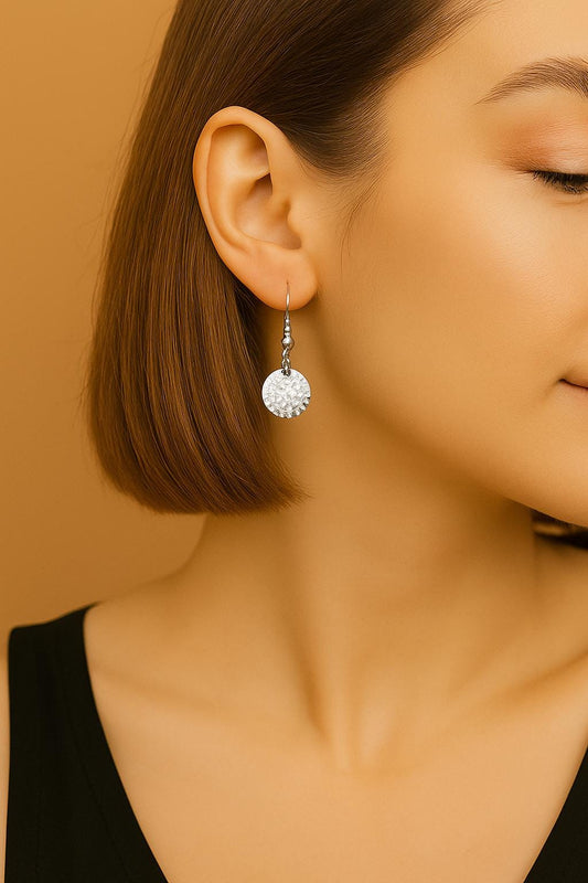 Close-up of a woman wearing a silver earring with a clear gemstone against a beige background